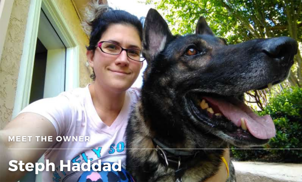 Selfie photo of Steph, a white woman with pink rimmed glasses, next to the large head of a German bred German shepherd with his tongue hanging out.